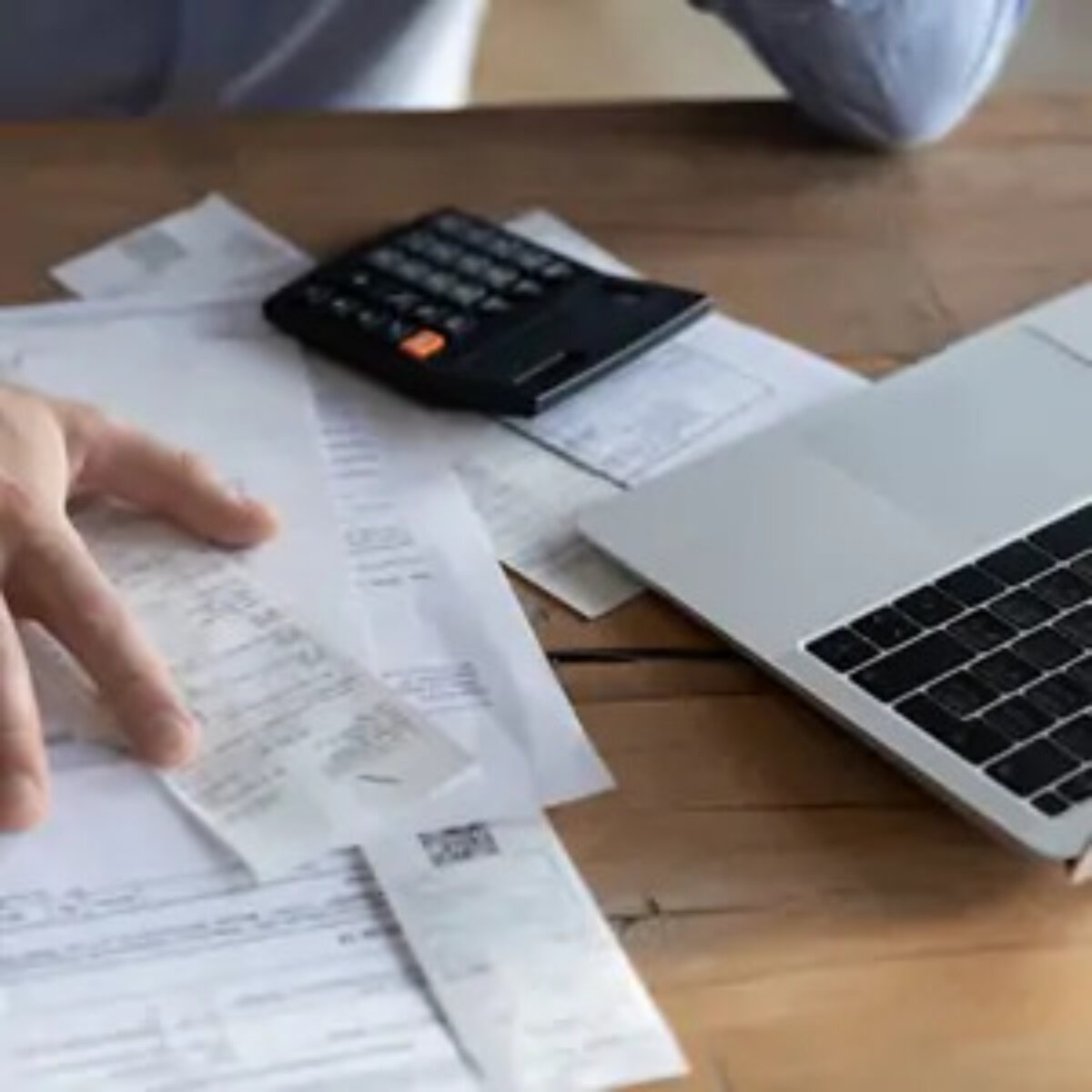 Businessman calculating VAT at desk with receipts, calculator and laptop