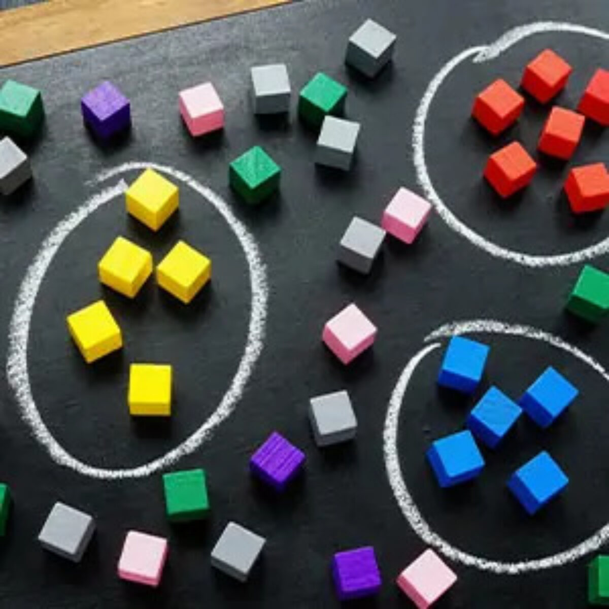 Three circles drawn on a chalk board, one with yellow wooden cubes inside, one with blue, and one with red, and cubes of different colours scattered outside the circles