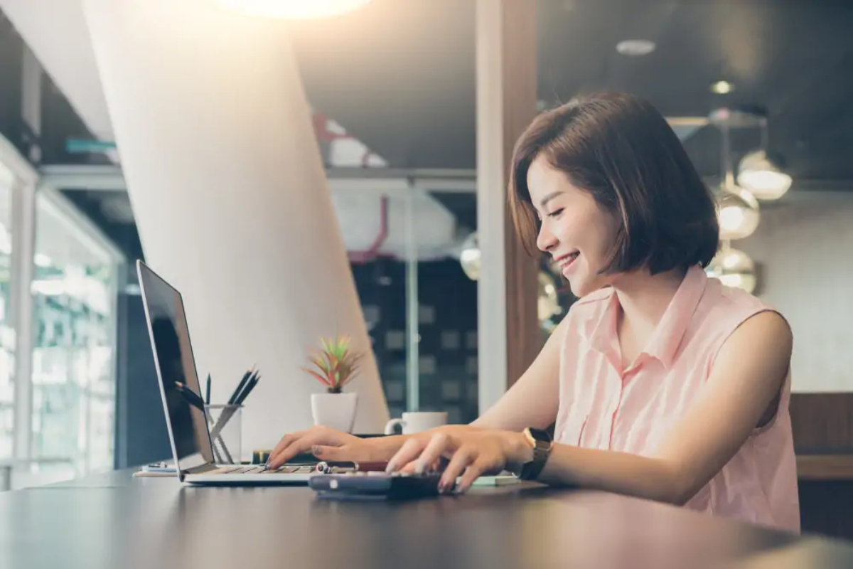 Businesswoman at desk using laptop with one hand and calculator with the other to work out personal allowance