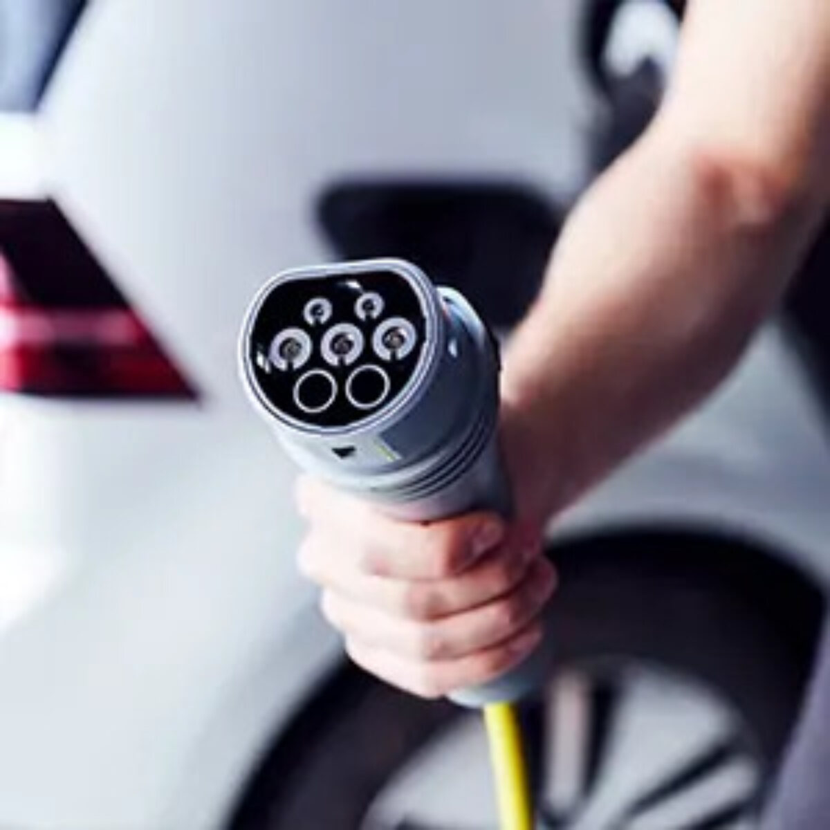 Hand holding charger in front of electric car