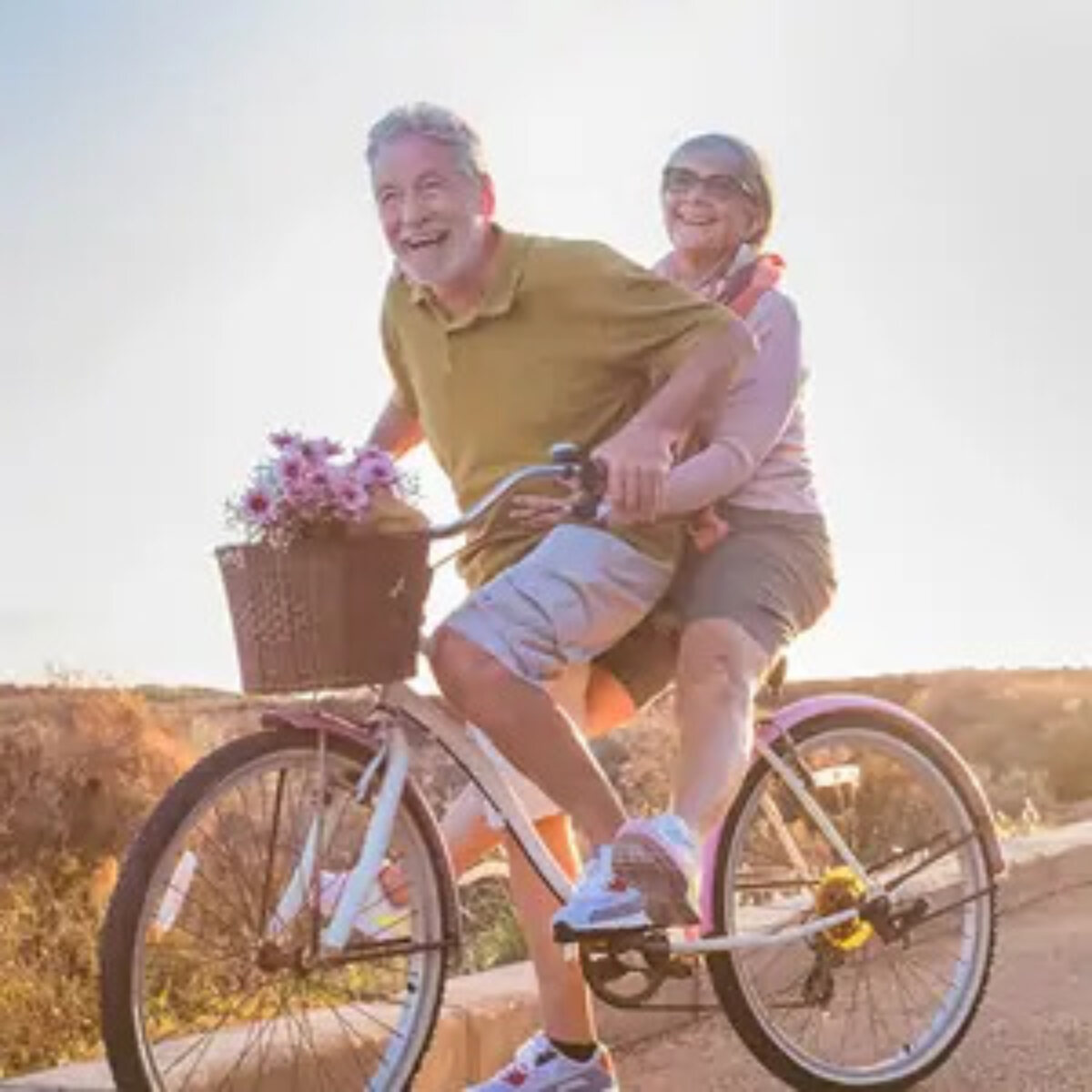 Elderly couple riding tandem bicycle in countryside and smiling