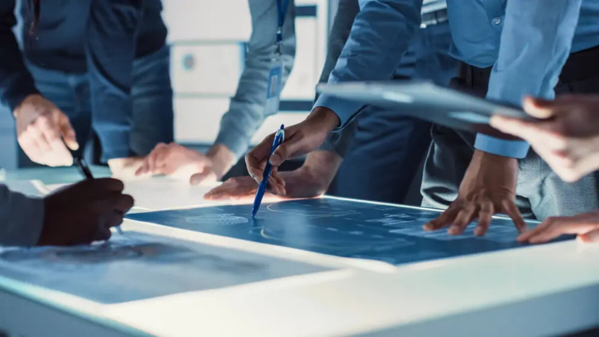 Businesspeople standing around illuminated table looking at R&D plans in a meeting