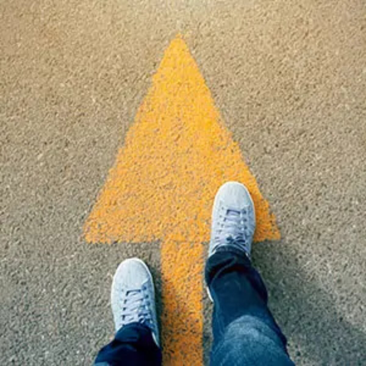 Two feet standing on a yellow arrow painted on the road pointing forwards