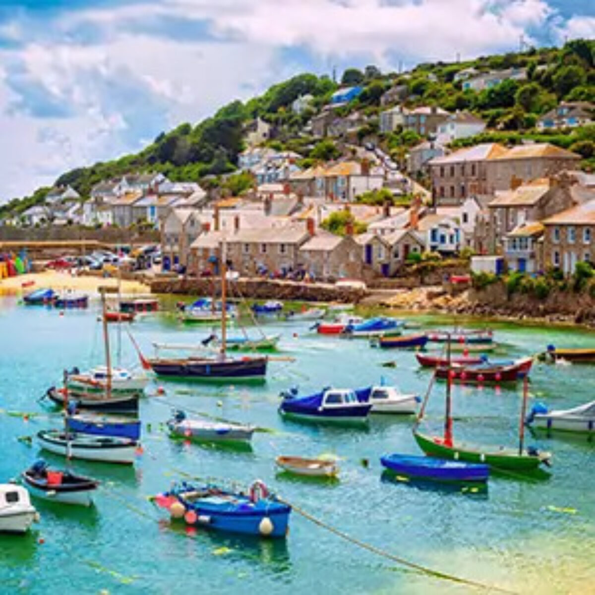 Sailboats in a sunny harbour by a beach with houses on a hill