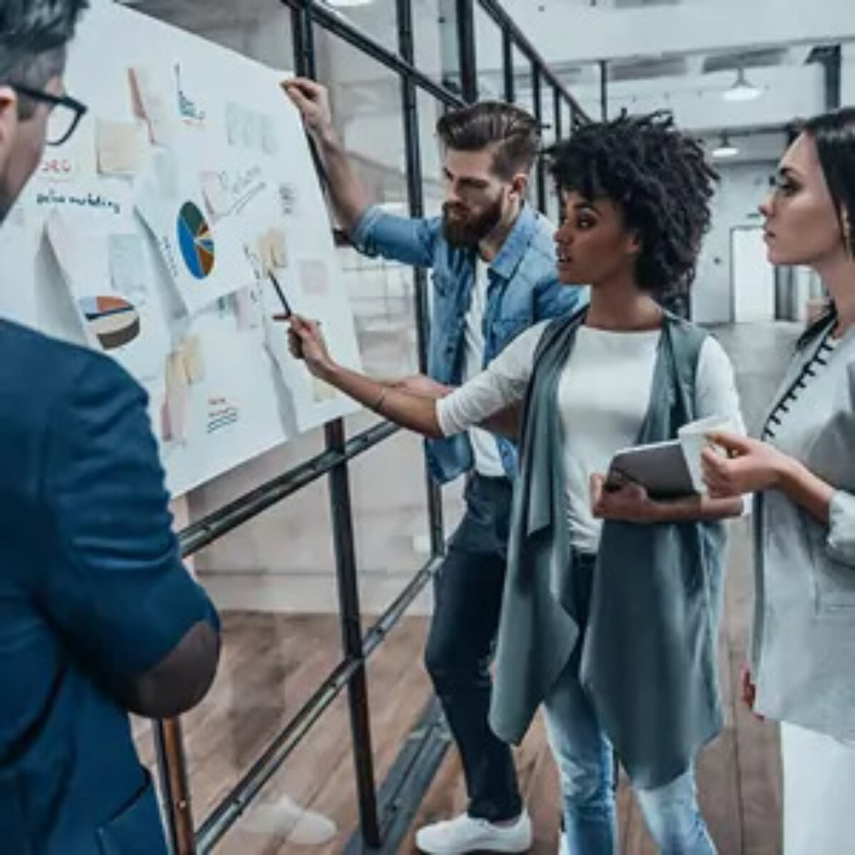 Businesspeople gathered around whiteboard in office with post-it notes and charts on it