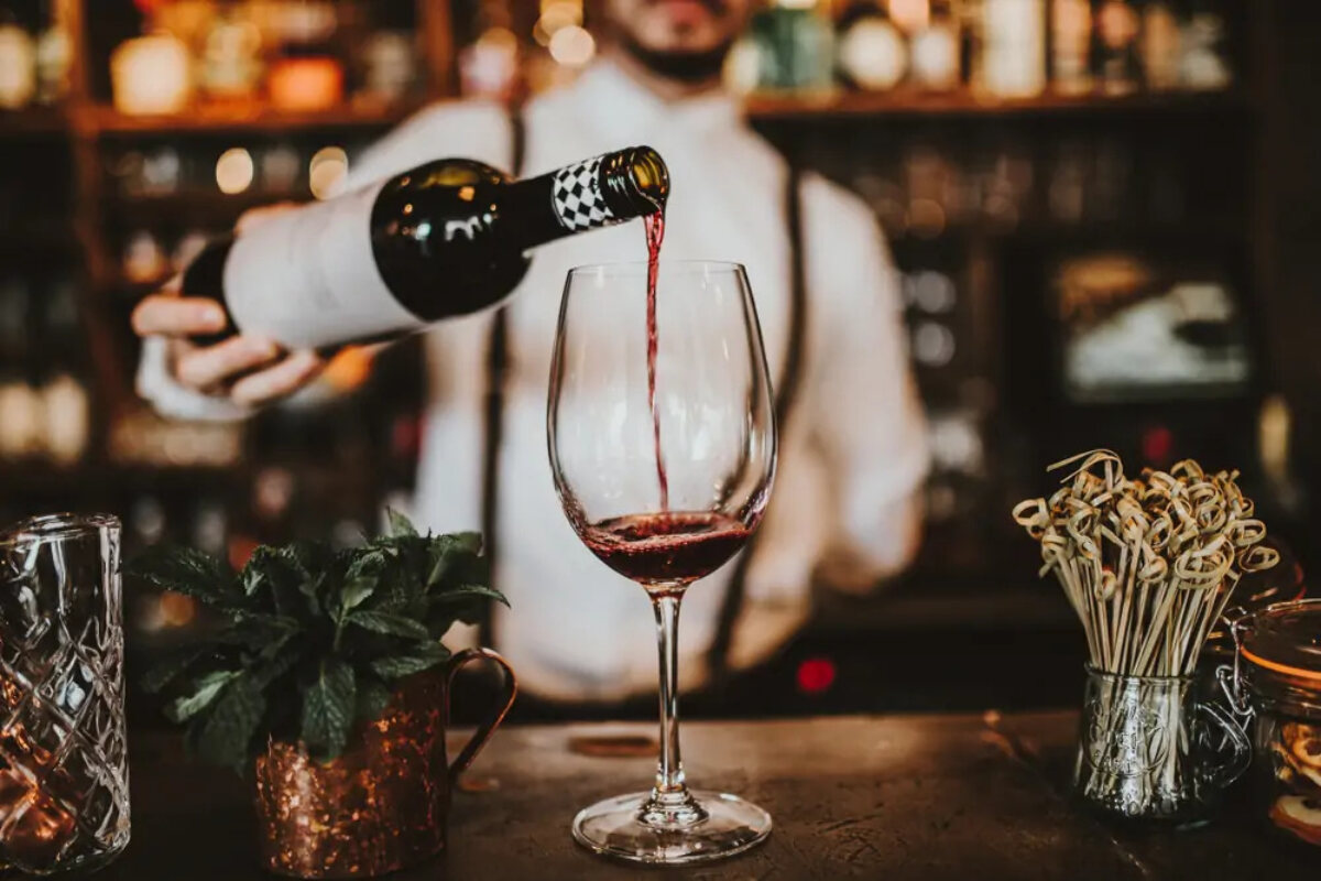 Bartender pouring red wone from bottle into glass