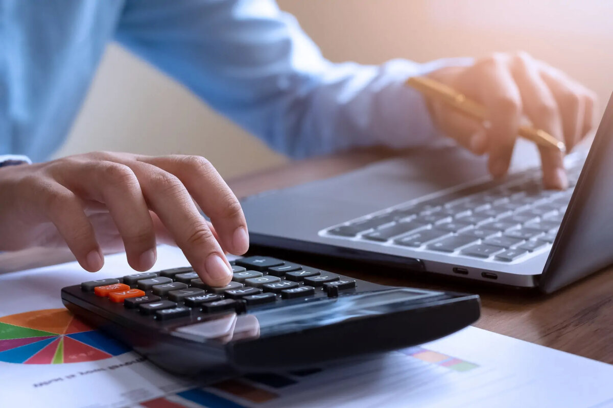 Businessperson using calculator with one hand and laptop with the other