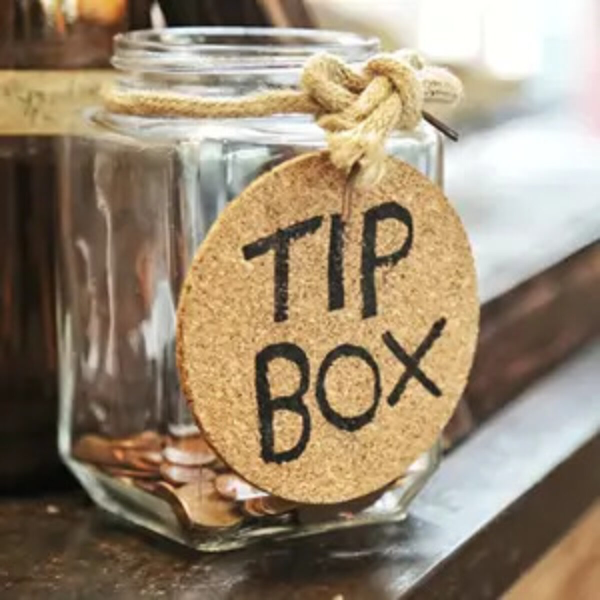 Jar with some coins inside on a ledge with a 'tip box' tag hanging from the rim