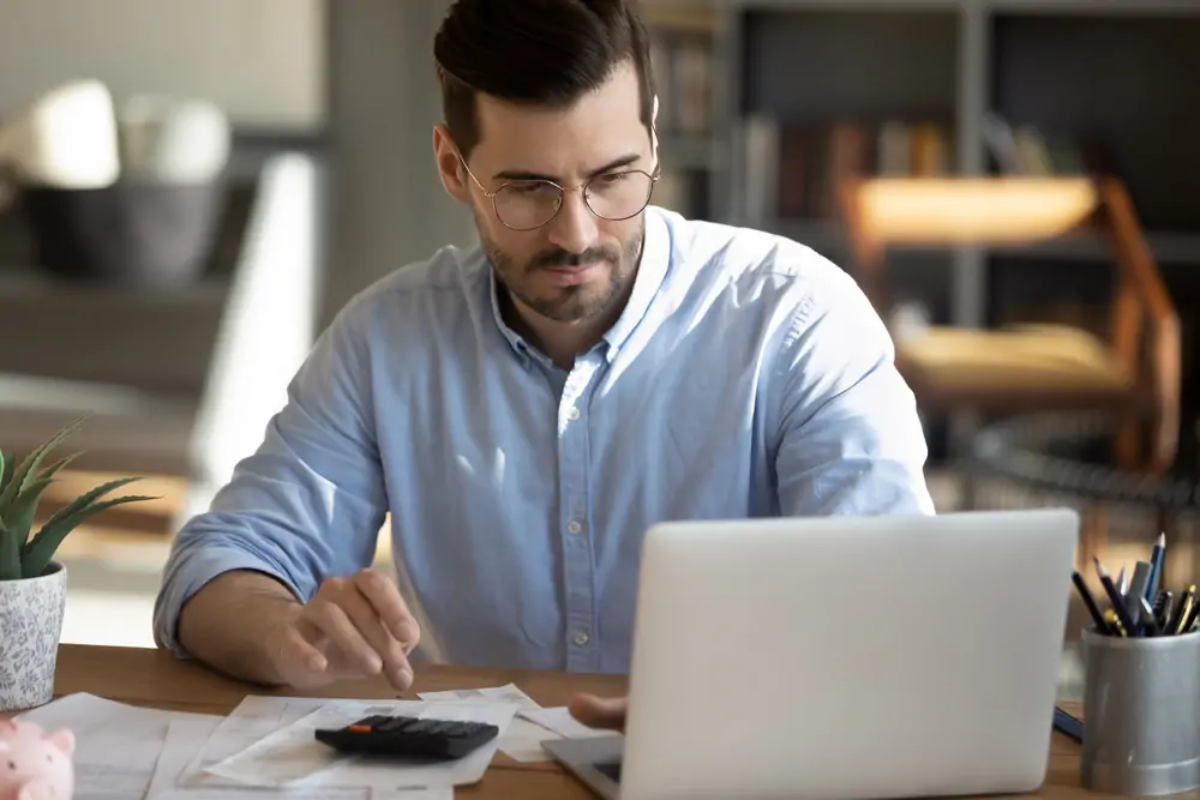 Businessperson sitting at desk looking at laptop and using calculator
