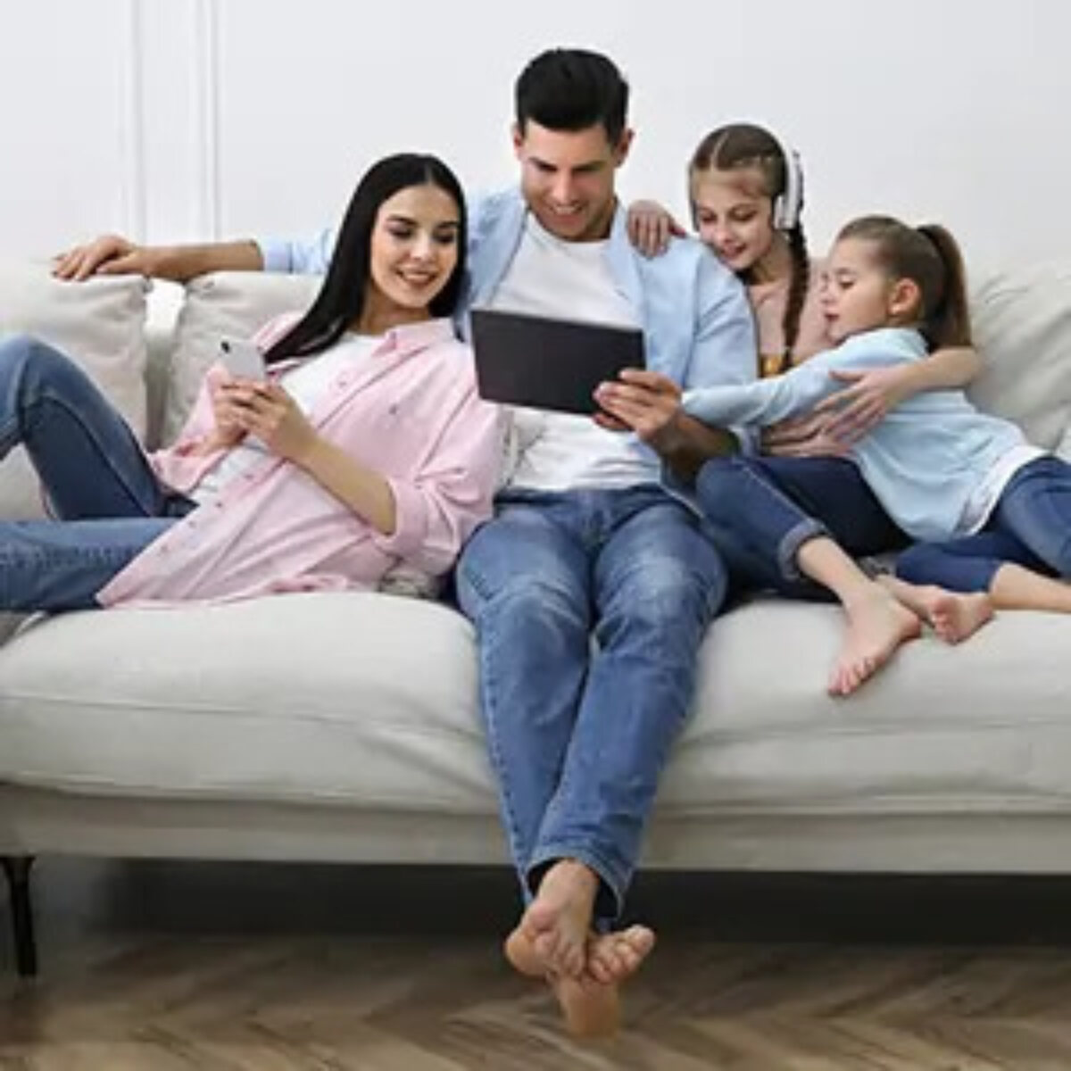 Young family sitting on sofa in home all looking at tablet that father is holding and smiling