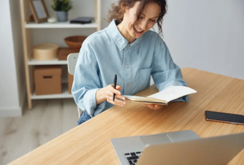 Businesswoman sitting at desk holding and smiling at open notebook