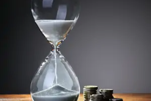 Sand timer halfway done next to four stacks of coins