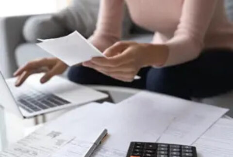 Woman sitting on sofa using laptop on coffee table calculating tax bill