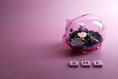Transparent piggy bank half-filled with coins, with three tiles spelling out 'SME' in front