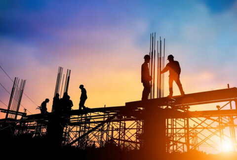 Construction workers standing on scaffolding as sun rises