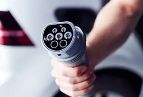 Hand holding charger in front of electric car