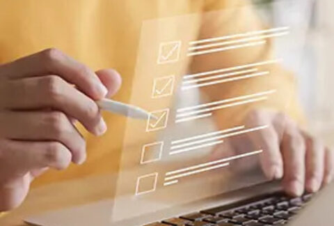 Businessman at desk working at laptop and ticking a box on a cartoon checklist overlayed