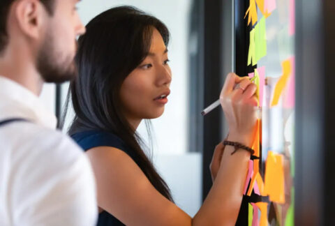 Businesswoman writing on post-it notes on wall t generate ideas for business goals