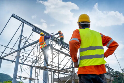 Two subcontractors working on scaffolding at construction site and one subcontractor standing watching them