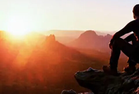 Climber resting on rocks looking out at sunrise