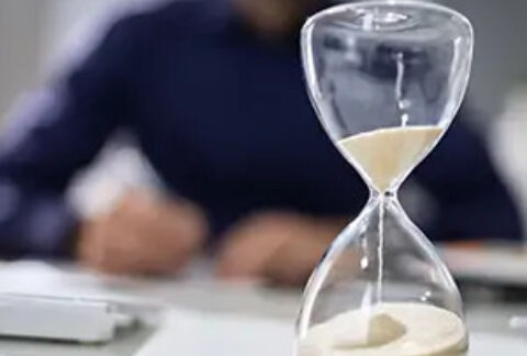 Sand timer in progress on desk with out-of-focus businessman in background