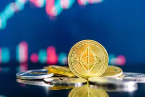 Crypto coin balanced on edge in front of pile of other crypto coins with crypto graph in background
