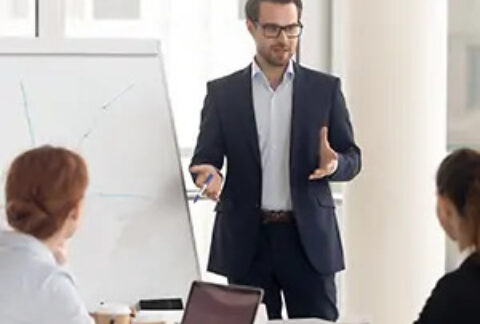 Businessman standing at flipchart talking to two seated colleagues