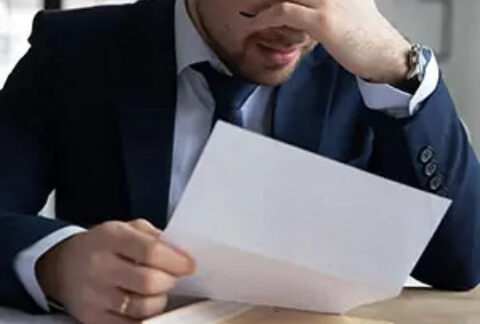Businessman at desk reading letter with hand on brow