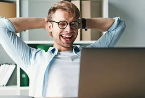 Businessman at desk smiling at laptop with hands behind head