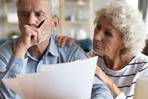 Elderly woman comforting elderly man who is holding pension document with fist to mouth looking into distance