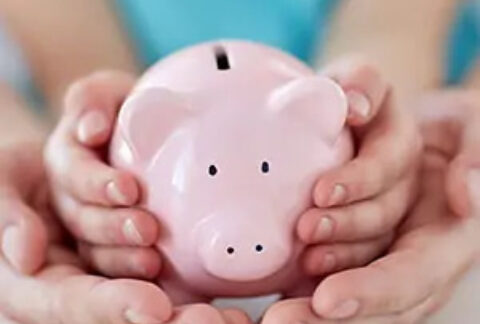 Adult's hands cupping child's hands holding piggy bank
