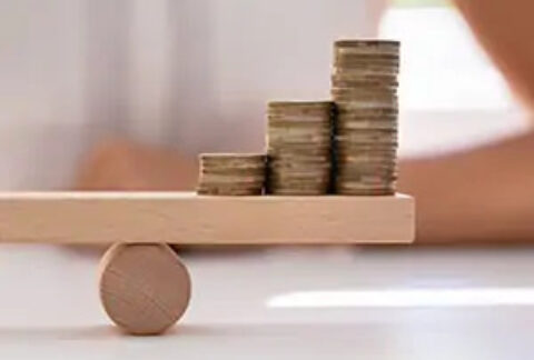 Three stacks of coins sitting on one side of a balanced miniature wooden seesaw