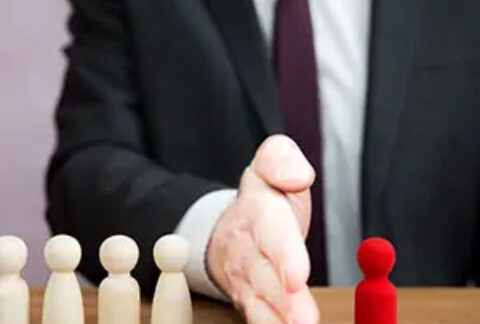 Businessman at table with hand out sideways separating four white figurines from one red figurine