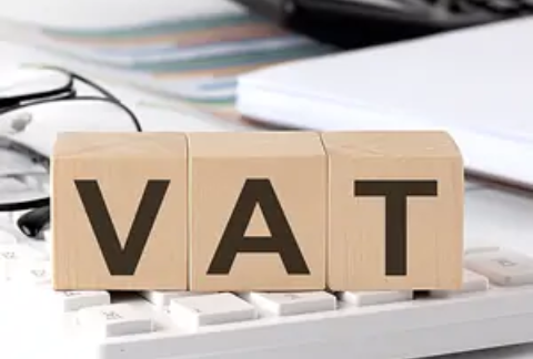 Wooden blocks with letters on them arranged on top of a calculator to spell out VAT