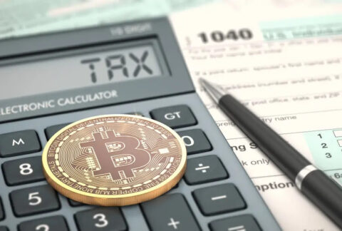 Bitcoin coin on top of a calculator reading 'tax' on screen