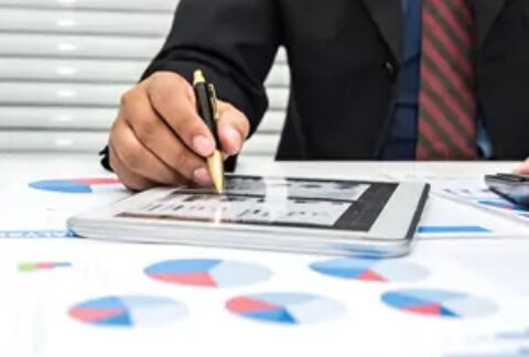 Businessman tapping tablet with stylus on desk covered in sheets of pie charts