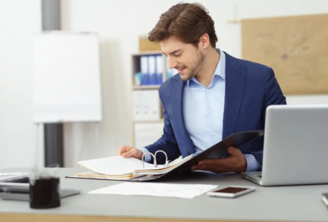 Businessman at desk looking at tax records in ring binder