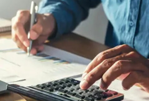 Businessman using calculator with one hand and holding pen to write on documents in the other