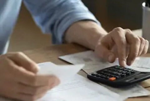 Businessman at desk using calculator and holding document to calculate tax payments