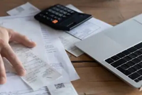 Businessman calculating VAT at desk with receipts, calculator and laptop