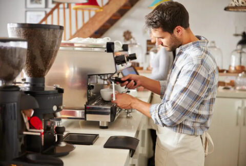 Hospitality worker using coffee machine behind coffee bar