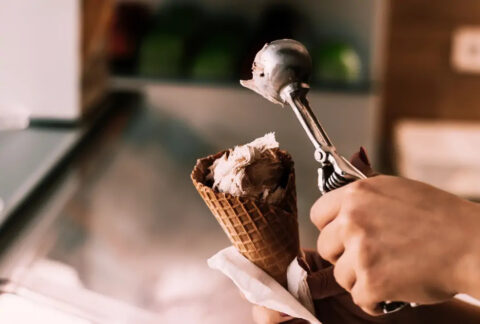 Hospitality worker scooping ice cream into a waffle cone