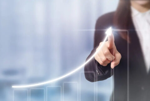 Businesswoman pointing at image of upwards arrow above an increasing bar chart