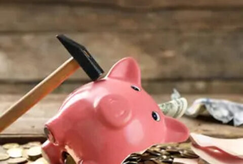 Broken piggy bank on ground with coins spilling out of side and a hammer resting on the other side