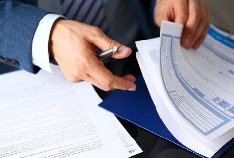 Businessman leafing through documents on clipboard with one hand and holing pen in the other