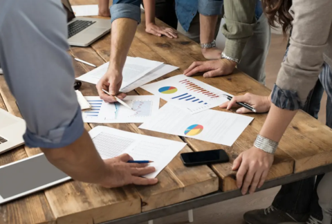 Businesspeople standing around table lookin at printed business performance graphs
