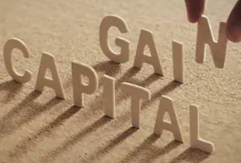 Hand placing paper letters upright on surface spelling out 'Capital Gains'