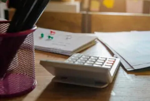 Calculator on desk next to pot of pencils and documents