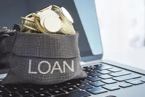 Small sack with 'loan' written on the front filled with gold coins, sitting on top of a laptop keyboard