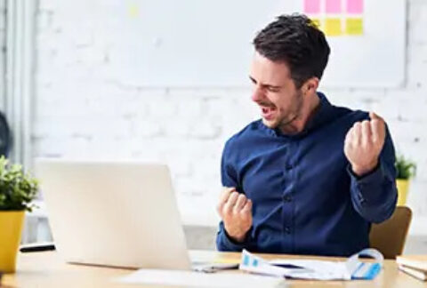Man celebrating at desk with open laptop